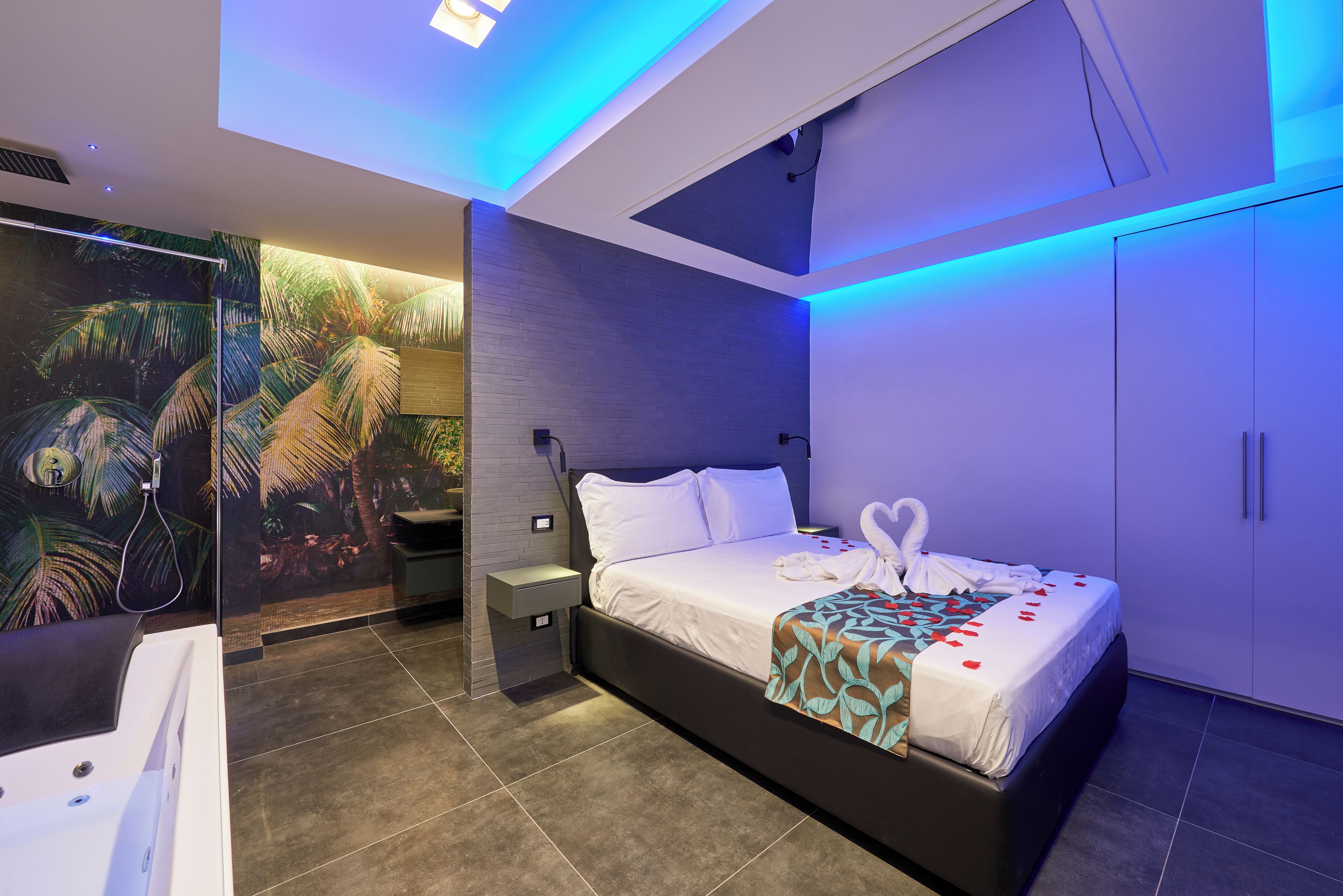 Un dormitorio moderno con una cama grande, una mesita de noche, televisor montado en la pared y un baño con ducha.