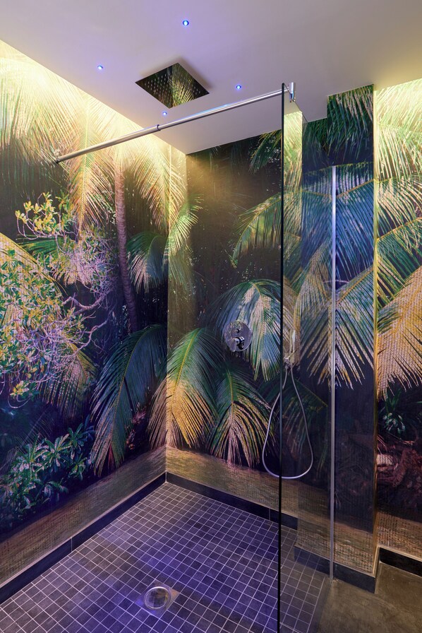 Un espace de douche clos par des parois de verre, dont les murs sont ornés d’une fresque aux motifs tropicaux.