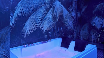 Une salle de bain moderne avec une grande baignoire, une fresque murale représentant des palmiers et un plafond doté d’un éclairage encastré.