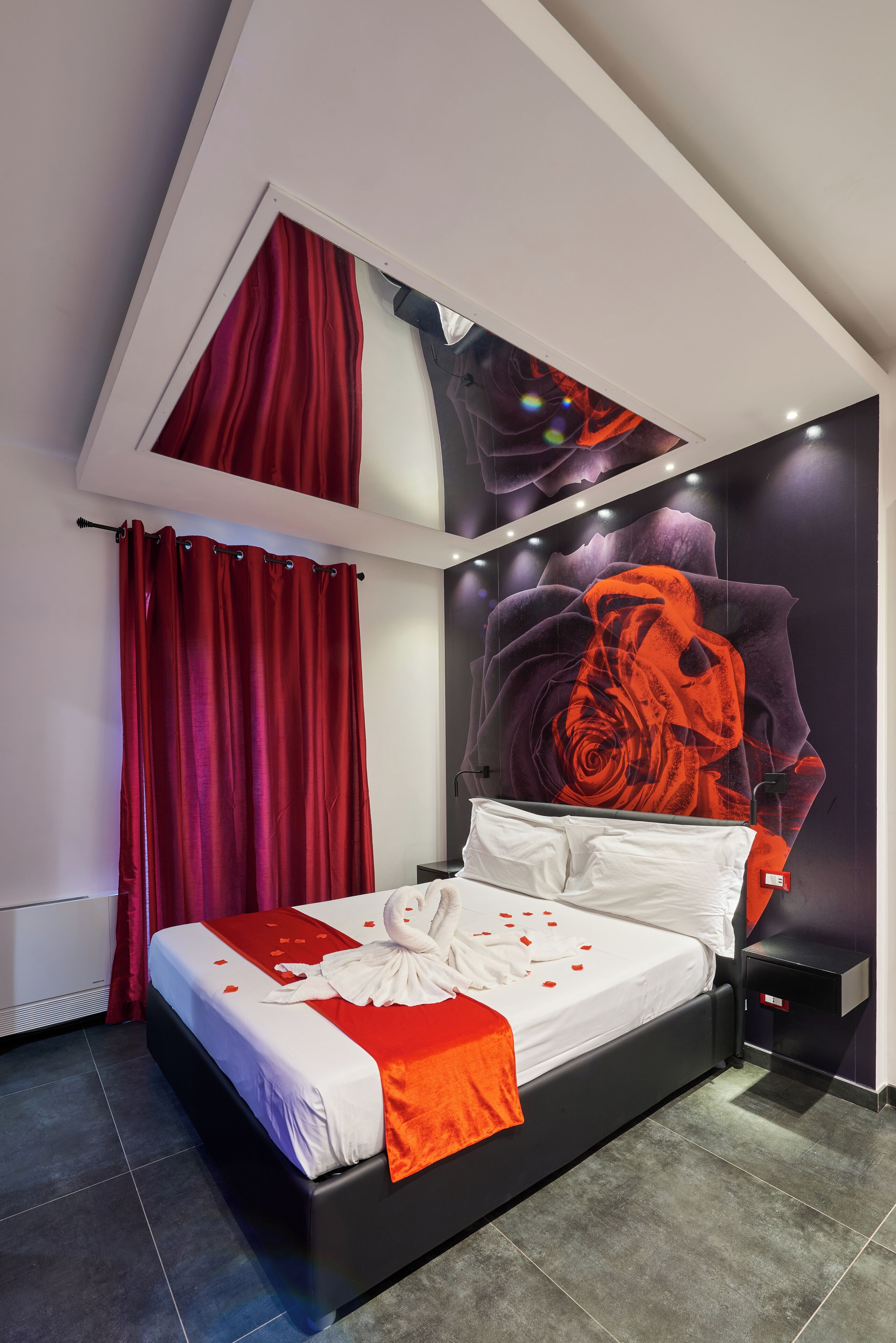 Een moderne slaapkamer met een bed, rode gordijnen, een groot muurdecor en een nachtkastje.
