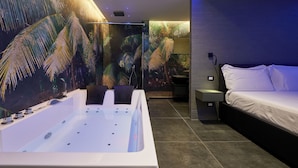 Un bagno moderno con una vasca da bagno ampia, una zona doccia e un letto con un comodino.