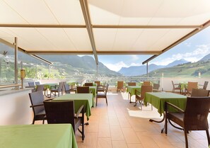 Un espace extérieur aménagé pour les repas, avec des tables et des chaises, un toit abrité et une vue sur les montagnes.
