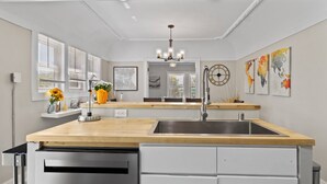 A modern kitchen with a wooden countertop, stainless steel sink, and white cabinetry. There is a chandelier, a map on the wall, and a window with blinds. - Charming 2BD W/ Parking 15 Mins from Downtown (Milwaukee)
