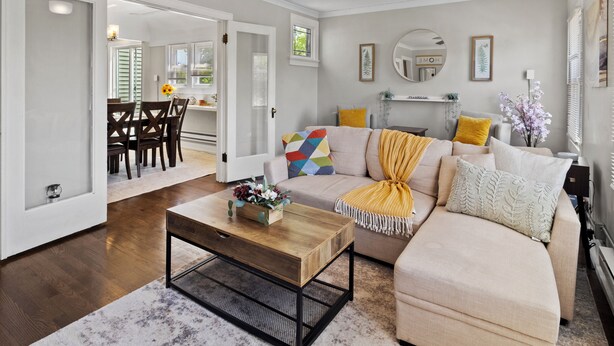A living room with a sofa, coffee table, and a ceiling fan. There is a dining area with a table and chairs visible through an open door. - Charming 2BD W/ Parking 15 Mins from Downtown (Milwaukee)