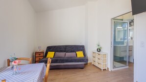 Un espacio habitable compacto con sofá, una mesa de comedor, un mueble pequeño y una puerta corredera de vidrio que da a un baño.
