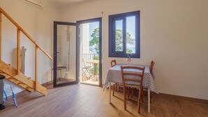 Una habitación con escalera de madera, una mesa con sillas, un ventanal y un equipo de aire acondicionado.