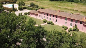 Um edifício cor-de-rosa com telhado em azulejos, rodeado por vegetação e piscina.