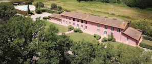 Ein pinkfarbenes Gebäude mit einem Ziegeldach, umgeben von viel Grün und einem Swimmingpool.