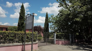 A gated entrance with a sign, a pink building, and tall trees.