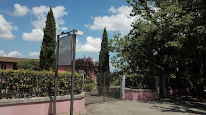 A gated entrance with a sign, a pink building, and tall trees.