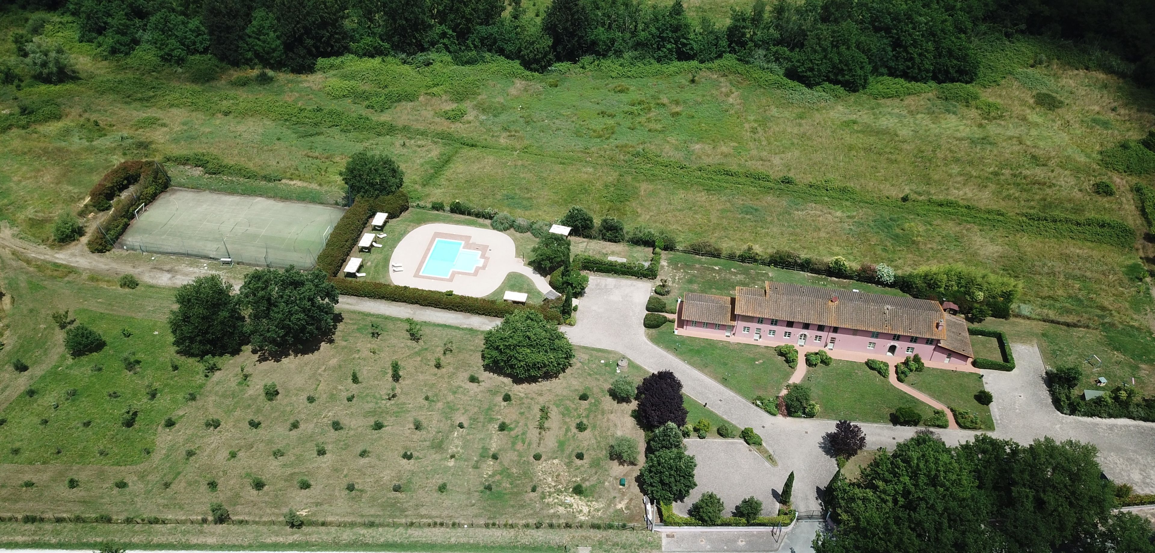 Vue aérienne d’une propriété dotée d’une piscine, d’un court de tennis et d’un grand bâtiment surmonté d’un toit en tuiles.