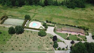 Vue aérienne d’une propriété dotée d’une piscine, d’un court de tennis et d’un grand bâtiment surmonté d’un toit en tuiles.