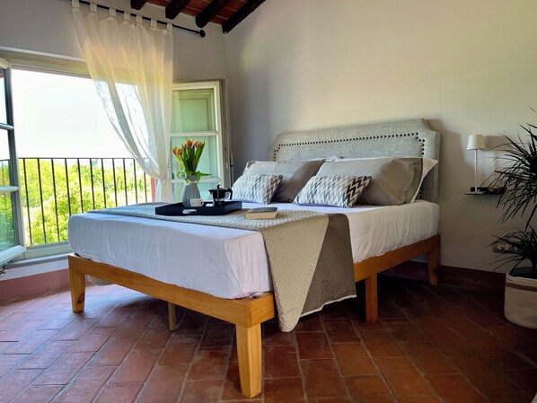 A bed with a headboard, a bedside table, a window with curtains, and a view of greenery outside.