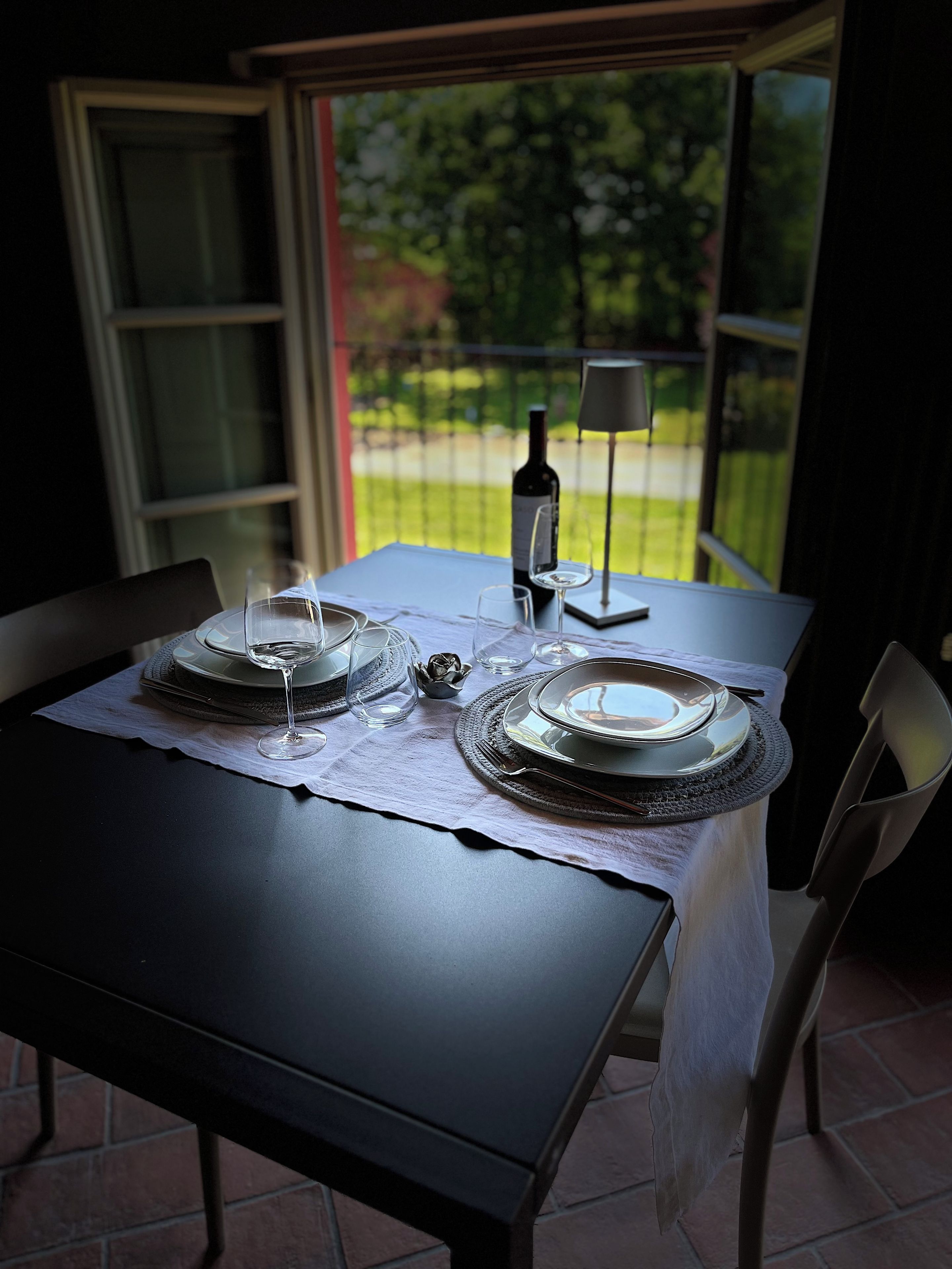Een gedekte tafel voor twee personen, met wijnglazen, een fles en een lamp.