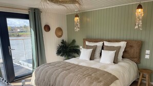 Un dormitorio con una cama grande, piso de madera, vista a través de una puerta corrediza y una lámpara colgante.