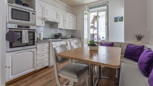 Una cocina moderna con armarios blancos, un microondas y una zona de comedor con mesa de madera y cojines morados.