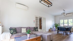 Una sala moderna con un sofá modular, una mesa de centro de vidrio, un comedor con mesa y sillas, y un ventanal que proporciona luz natural.