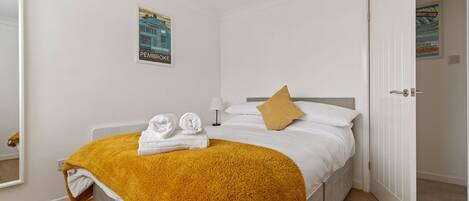 A bedroom with a bed, a yellow blanket, two towels, a pillow, a poster on the wall, and a door.