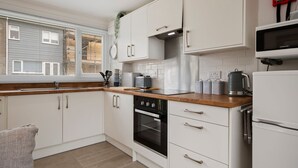 A modern kitchen with white cabinets, a wooden countertop, a built-in oven, a microwave, and a window with blinds. - Dewis Da - Short walk from beach, parking (Freshwater East)
