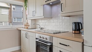 A modern kitchen with white cabinets, a wooden countertop, a built-in oven, and a coffee maker. - The Retreat - Short walk from beach, parking (Freshwater East)