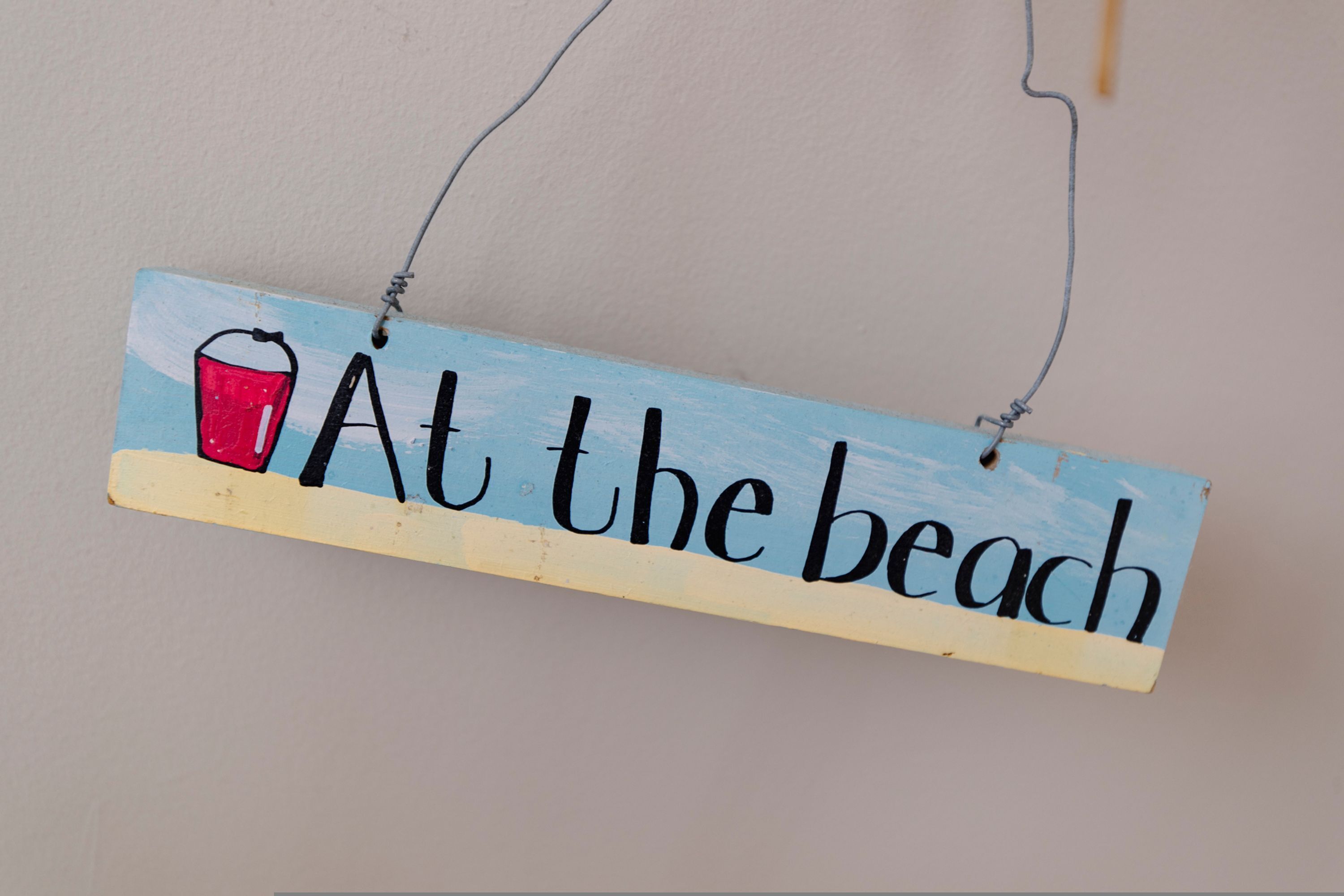 Een houten bord met de tekst 'Aan het strand' en een rode emmer afbeelding.