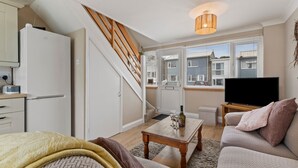 A cozy living room with a sofa, a coffee table, a TV, and a staircase leading to an upper level. - The Retreat - Short walk from beach, parking (Freshwater East)