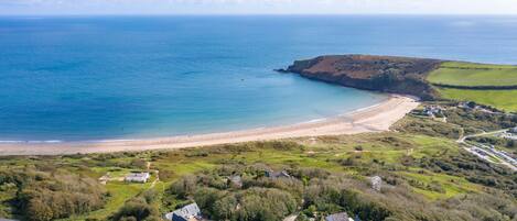 An aerial view of a coastal area with a beach, green fields, and residential buildings.