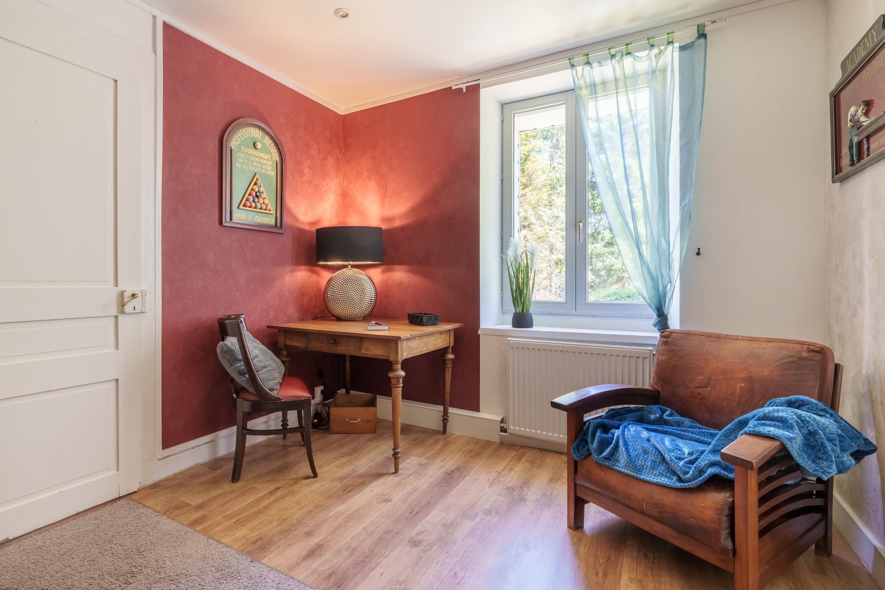 A room with a wooden desk, a chair, a radiator, and a window with curtains.