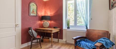 A room with a wooden desk, a chair, a radiator, and a window with curtains.