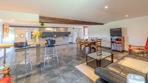A modern kitchen with dark tiles, a dining area with wooden chairs, and a living room with a leather sofa. - Les Coquelicots - A 30 min de Roanne (Régny)