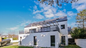 A modern two-story house with a flat roof, large windows, and a covered outdoor area.
