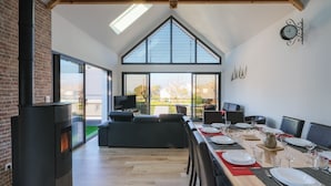 A dining area with a long table set for six, a fireplace, and a large window with a view of the outdoors.