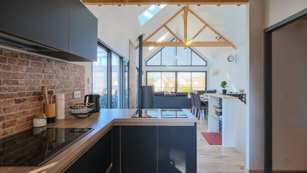 A modern kitchen with a brick wall, black cabinets, and a wooden ceiling.
