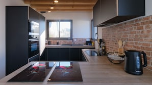 A modern kitchen with black cabinets, a wooden countertop, and a brick wall.