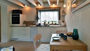 A compact kitchen with white cabinets, a wooden ceiling, and a window providing natural light.