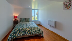 A bedroom with a bed, a nightstand, a lamp, a window, and a radiator. - Le Clos de Verpierre - Appart avec Jardin (Régny)