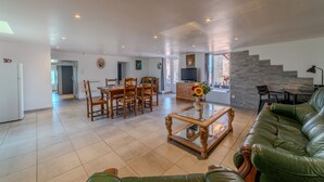 A spacious living area with a green leather sofa, wooden dining table, and a TV. - Le Clos de Verpierre - Appart avec Jardin (Régny)