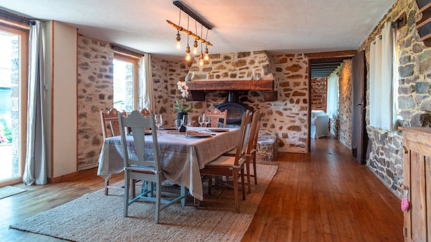 A dining area with a stone wall, wooden table, and chairs. - La Jasserie - Jardin de 1800 m² et terrasse (Argol)
