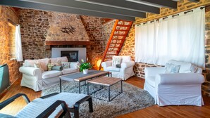 A cozy living room with stone walls, a fireplace, white sofas, and a wooden coffee table. - La Jasserie - Jardin de 1800 m² et terrasse (Argol)