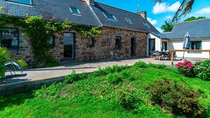 A stone house with a sloped roof, a patio with outdoor furniture, and a garden with various plants. - La Jasserie - Jardin de 1800 m² et terrasse (Argol)