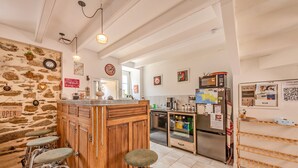 A kitchen with a bar area, stone wall, and various kitchen appliances. - Ti Riboul - proche plage (Douarnenez)