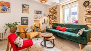 A cozy living room with a green sofa, red armchair, and a round coffee table. There are various framed pictures and a stone wall. - Ti Riboul - proche plage (Douarnenez)