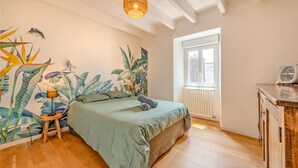 A bedroom with a bed, a small stool, a wall mural, a window, and a radiator. - Ti Riboul - proche plage (Douarnenez)