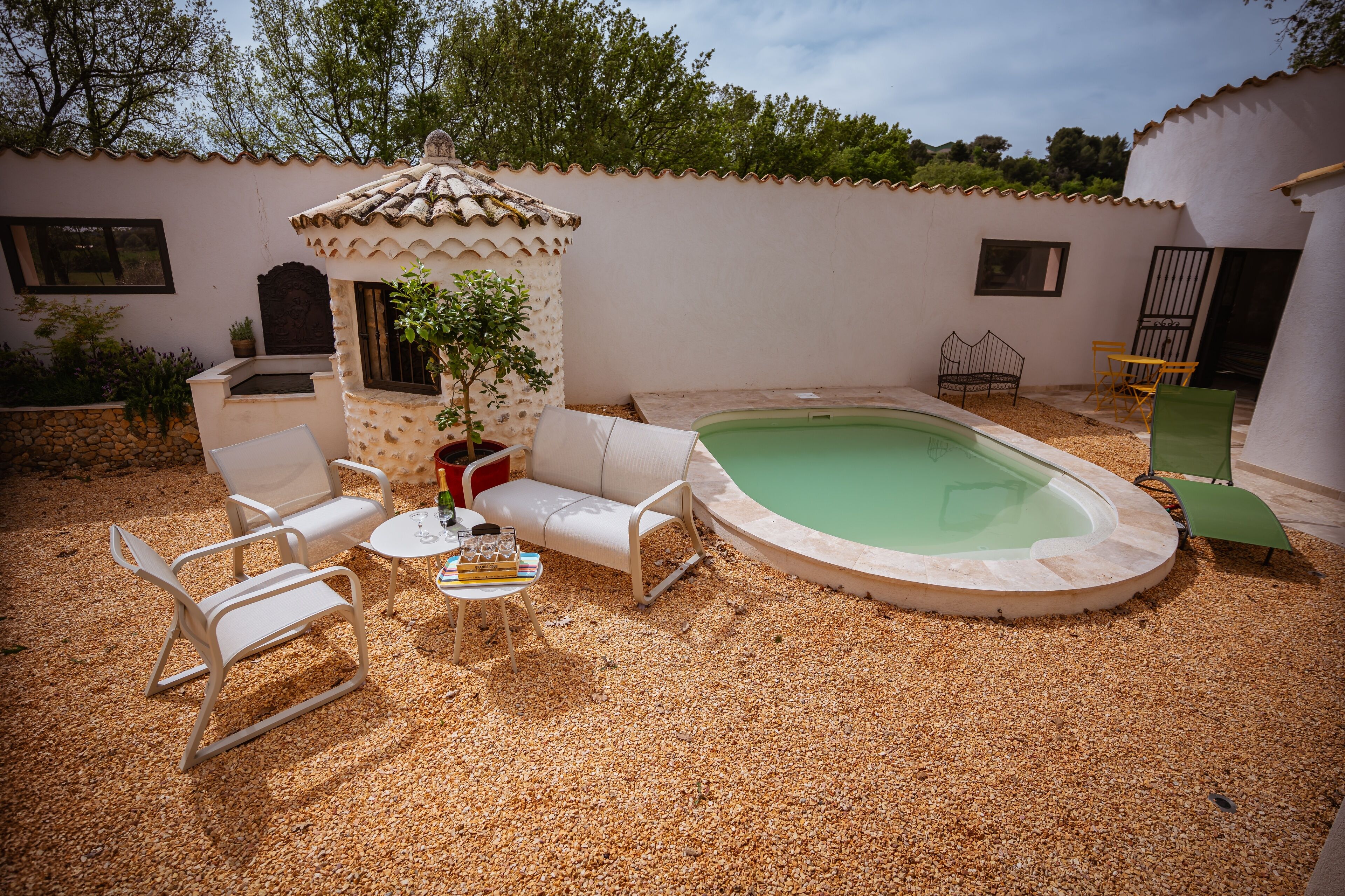 Un espace piscine agrémenté d’une petite terrasse, de chaises longues blanches, d’une table avec des livres et d’une plante en pot.