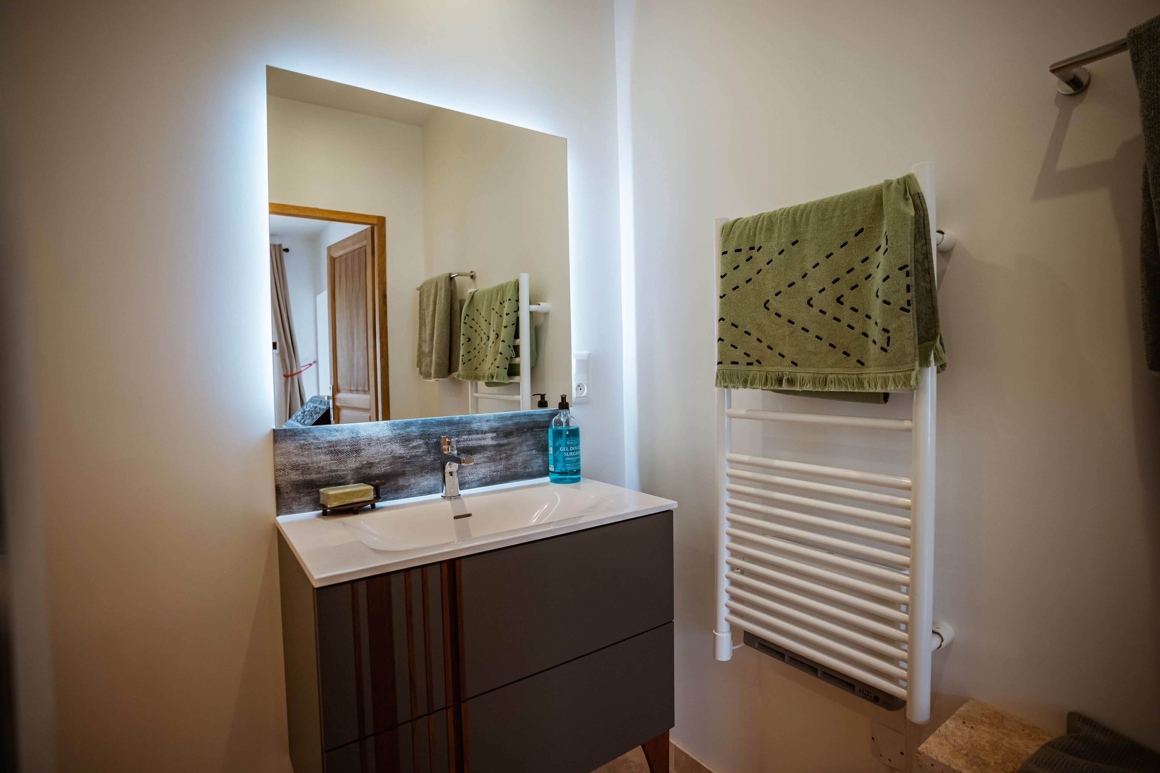 A bathroom with a white sink, dark cabinetry, a mirror with a wooden frame, a towel rack with a green towel, and a white radiator.