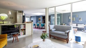 A modern living room with a sofa, a coffee table, and a TV. There is a dining area with a table and chairs in the background.