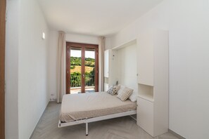 Un dormitorio con cama, armario, ventana con cortinas y vistas a la vegetación.