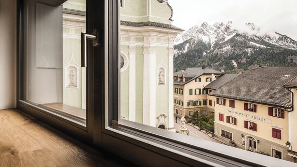 Vista desde una ventana de un edificio con un letrero que dice "SCHWARZER ADLER" y montañas al fondo.