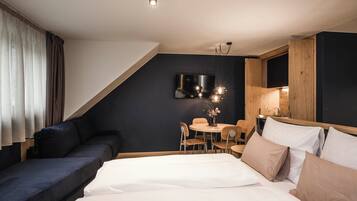 Une chambre d’hôtel moderne comprenant un lit, un canapé, une table à manger avec des chaises, un téléviseur fixé au mur et un meuble en bois.