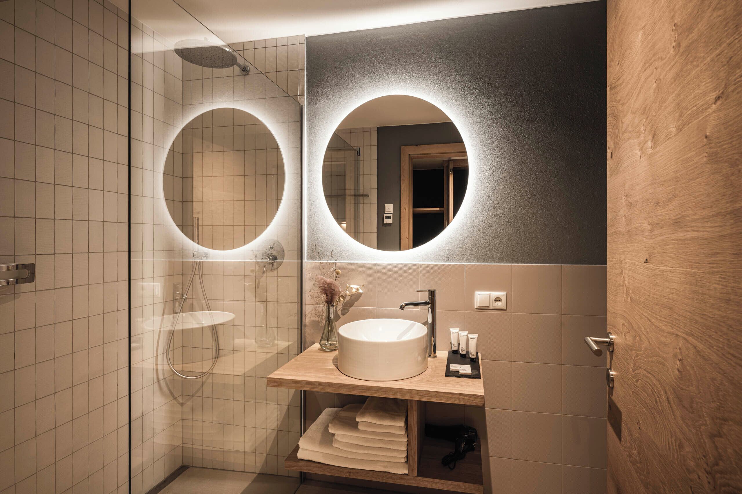 A modern bathroom with a large mirror, a round sink, and a glass-enclosed shower.